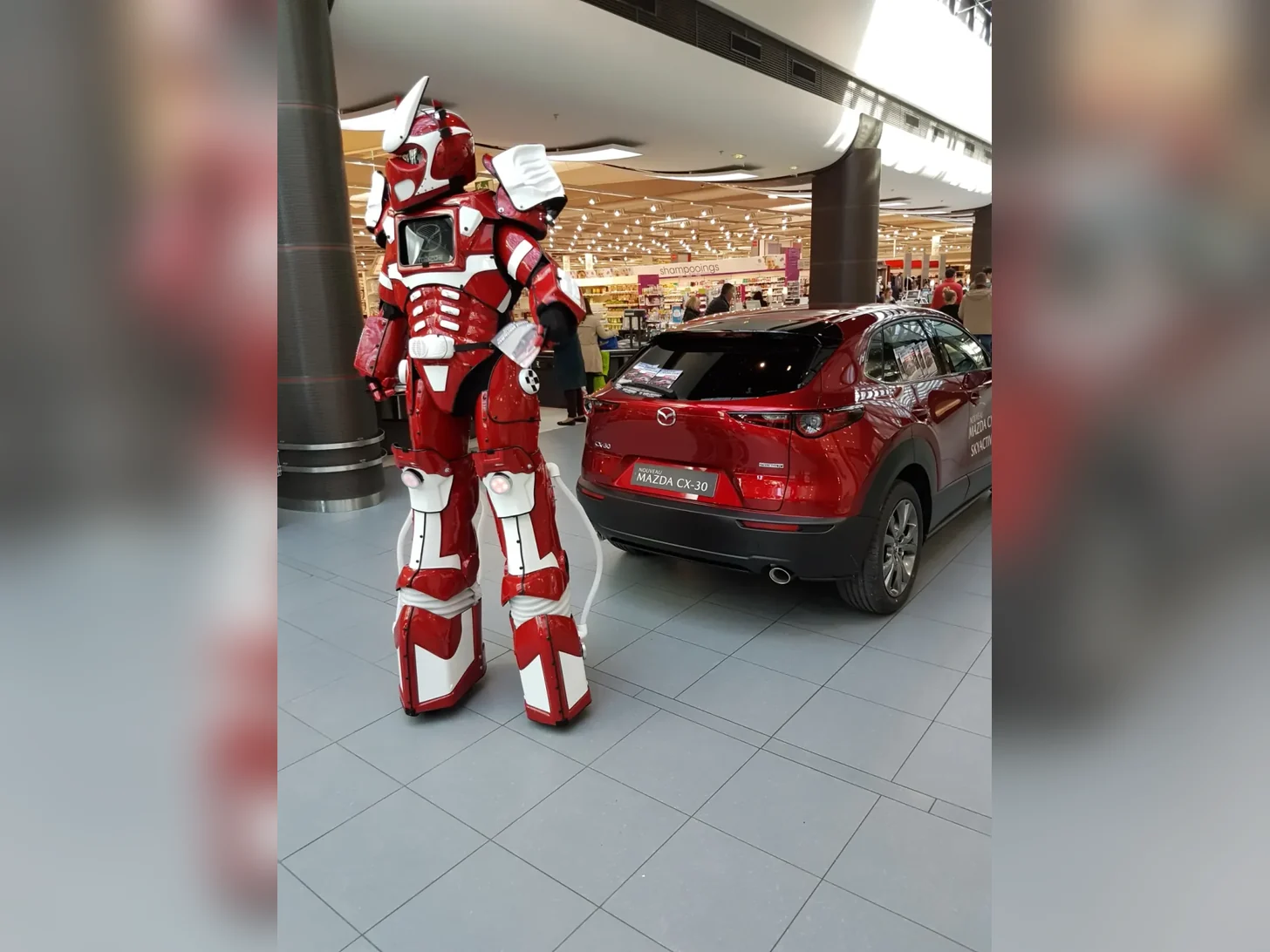 Robot LED rouge près d’un véhicule exposé en galerie marchande