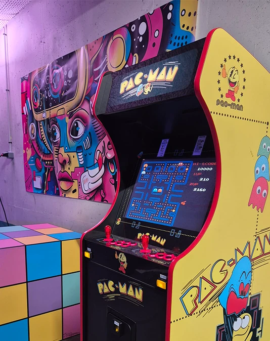 Borne arcade Pac-Man jaune dans une salle de jeux rétro avec néons muraux