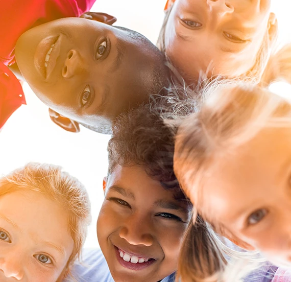 Cinq enfants souriants vus en plongée formant un cercle serré et regardant vers le bas