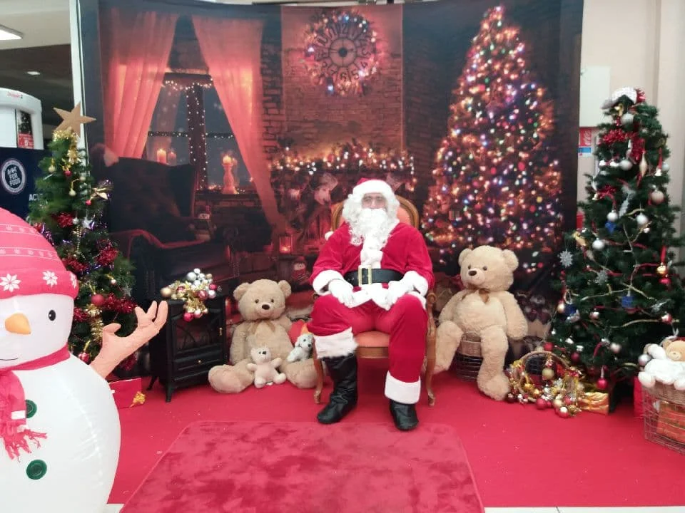 Stand du Père Noël By Anim avec décor de cheminée, sapins et oursons en peluche dans une galerie marchande